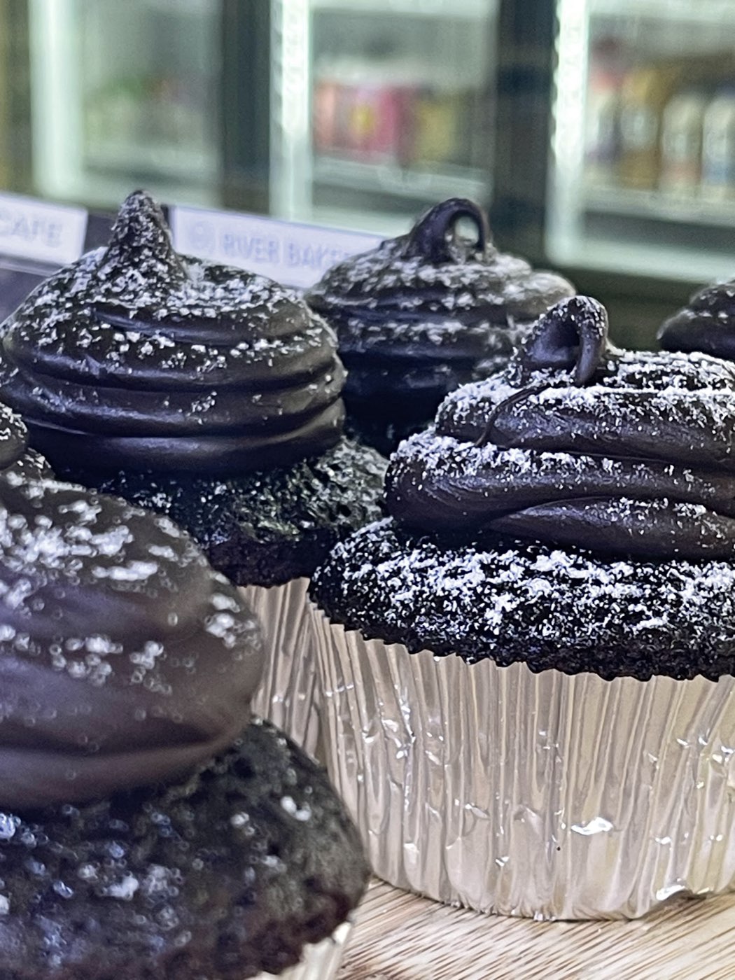 Chocolate cupcakes with swirls of dark icing dusted with icing sugar, in foil cases