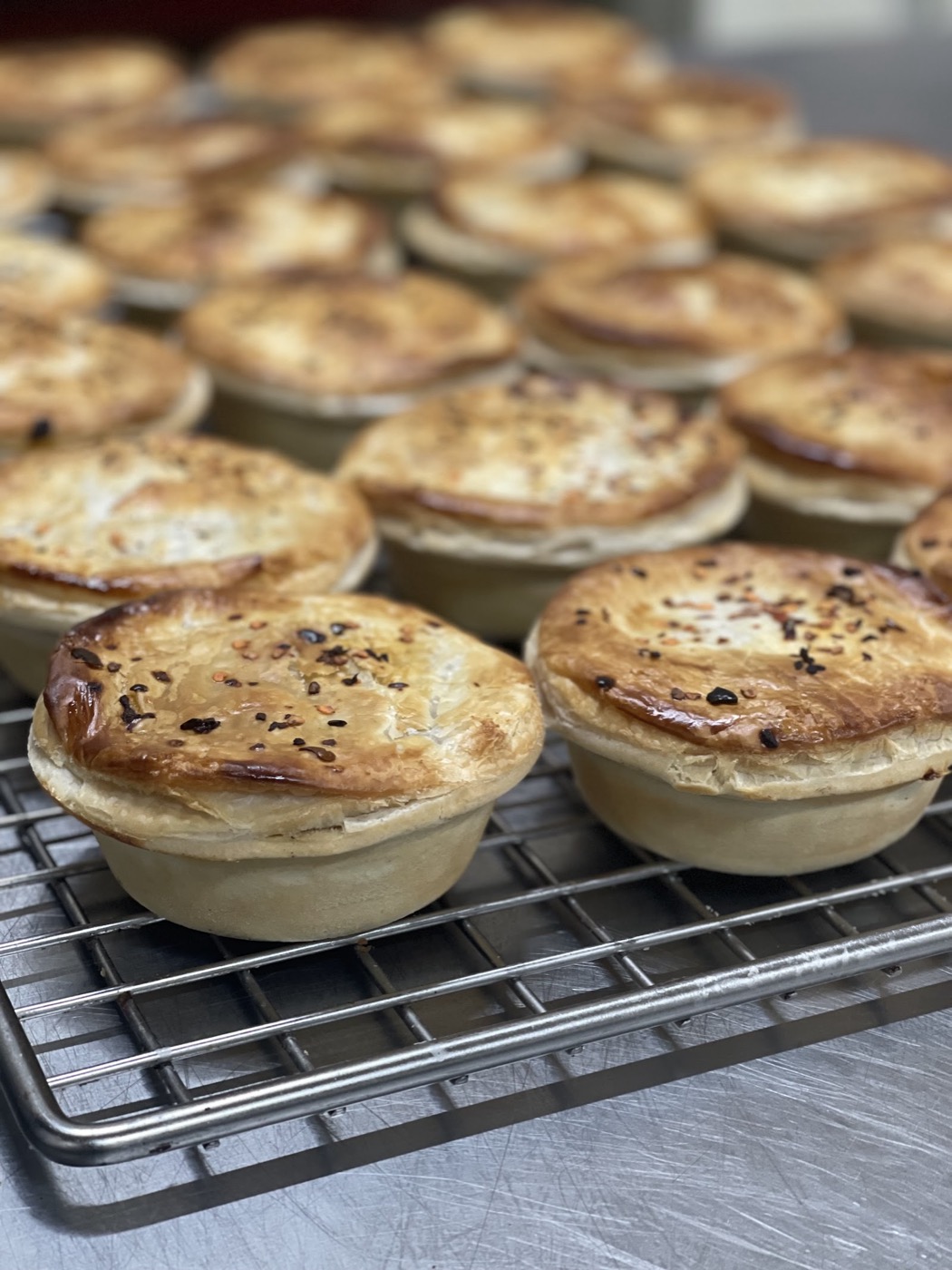 Rows of golden-brown individual pies with crimped tops, cooling on a wire rack