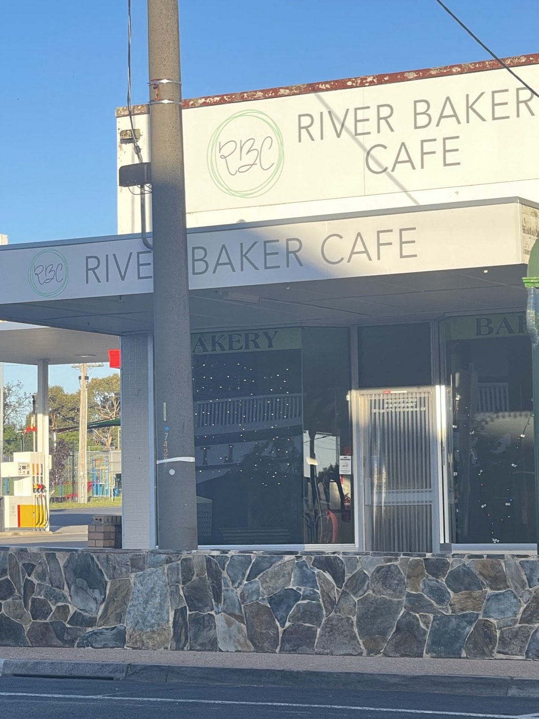 The bakery's front, with the River Baker Cafe name on the sign above a verandah and a stone-clad base, under a blue sky
