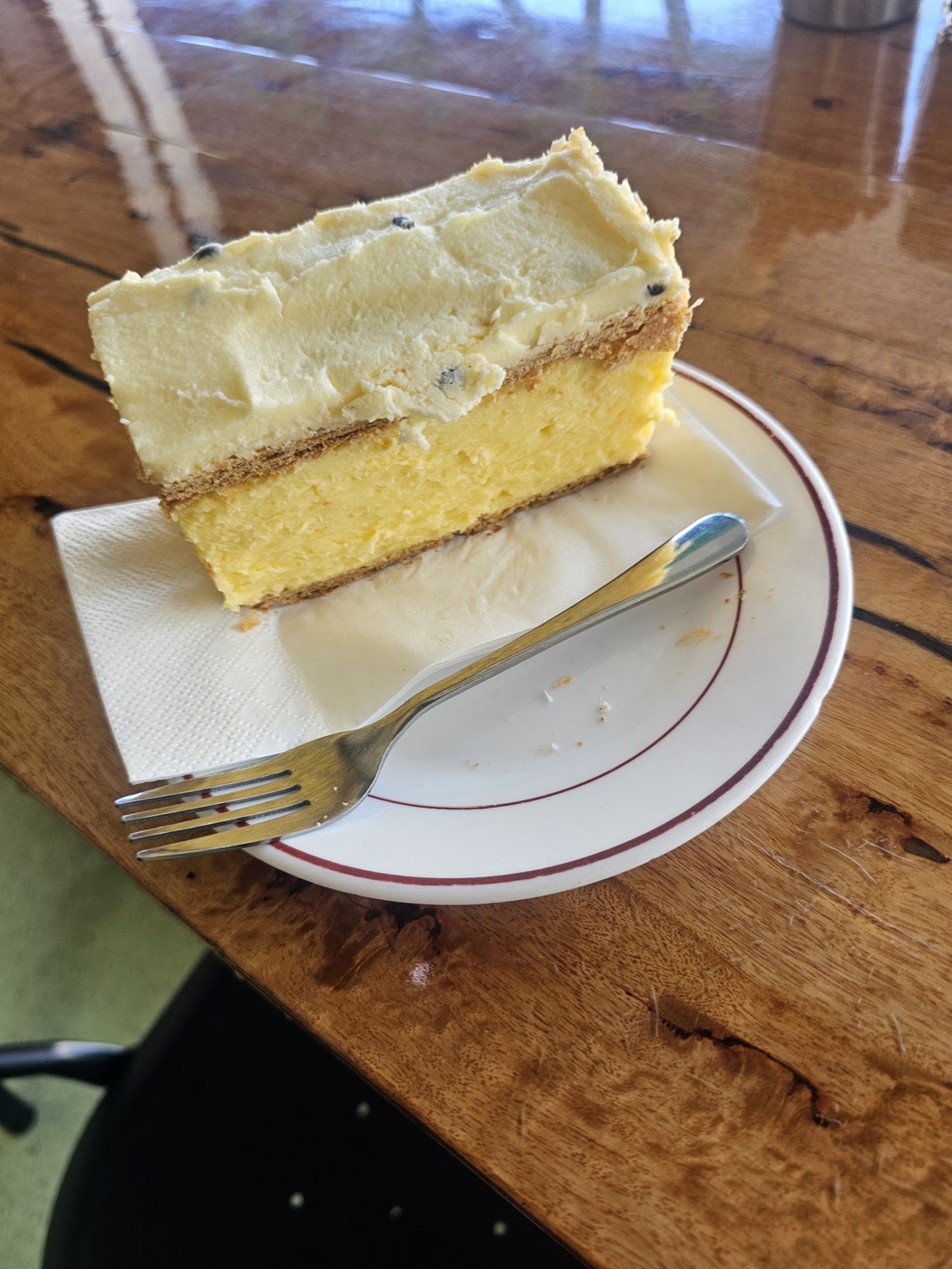 A thick slice of vanilla slice with a pale custard filling and yellow icing, on a white plate with a fork